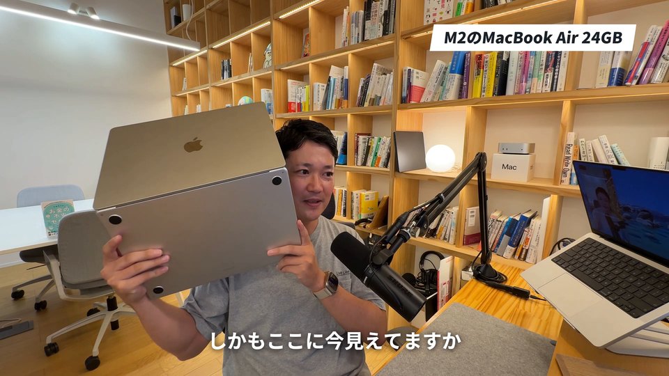 MacBookを持って話す講師の画面。下に白い字幕「しかもここに今見えてますか」、右上に見出し「M2のMacBook Air 24GB」